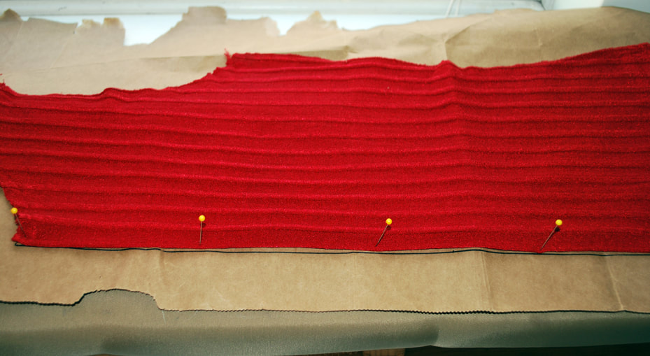 The back of a red top folded in  half with the folded edge pinned to a straight drawn-in line.