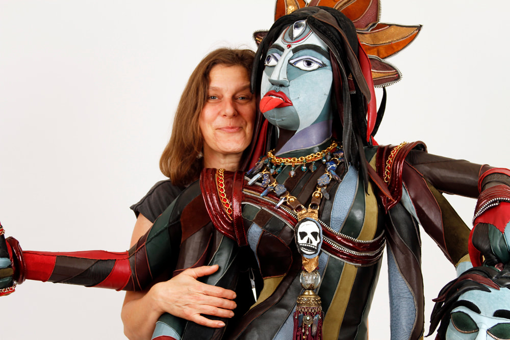 A woman holds the arms of a colorful representation of the goddess Kali. Kali is made of multicolored leather, and her red tongue sticks out at the camera.