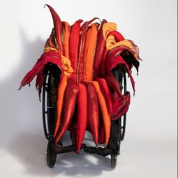 A red, orange, and gold padded wheelchair seat cover on a manual chair.