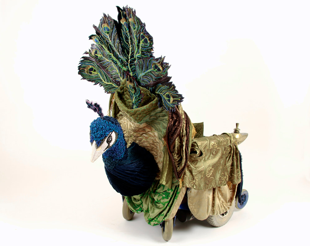 A mobility scooter is dressed as an Art Nouveau peacock. The peacock is blue, green, and gold, and he stares out at us from the back of the scooter.