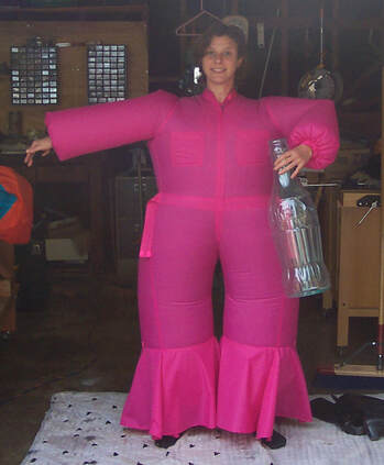 Woman in a bright pink inflatable jumpsuit holding an oversized soda bottle