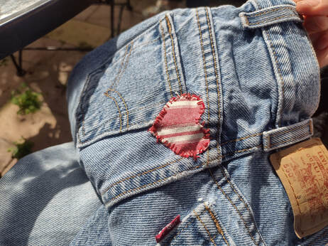 Faded jeans with a hand sewn red and white striped heart patch over the side of a back pocket