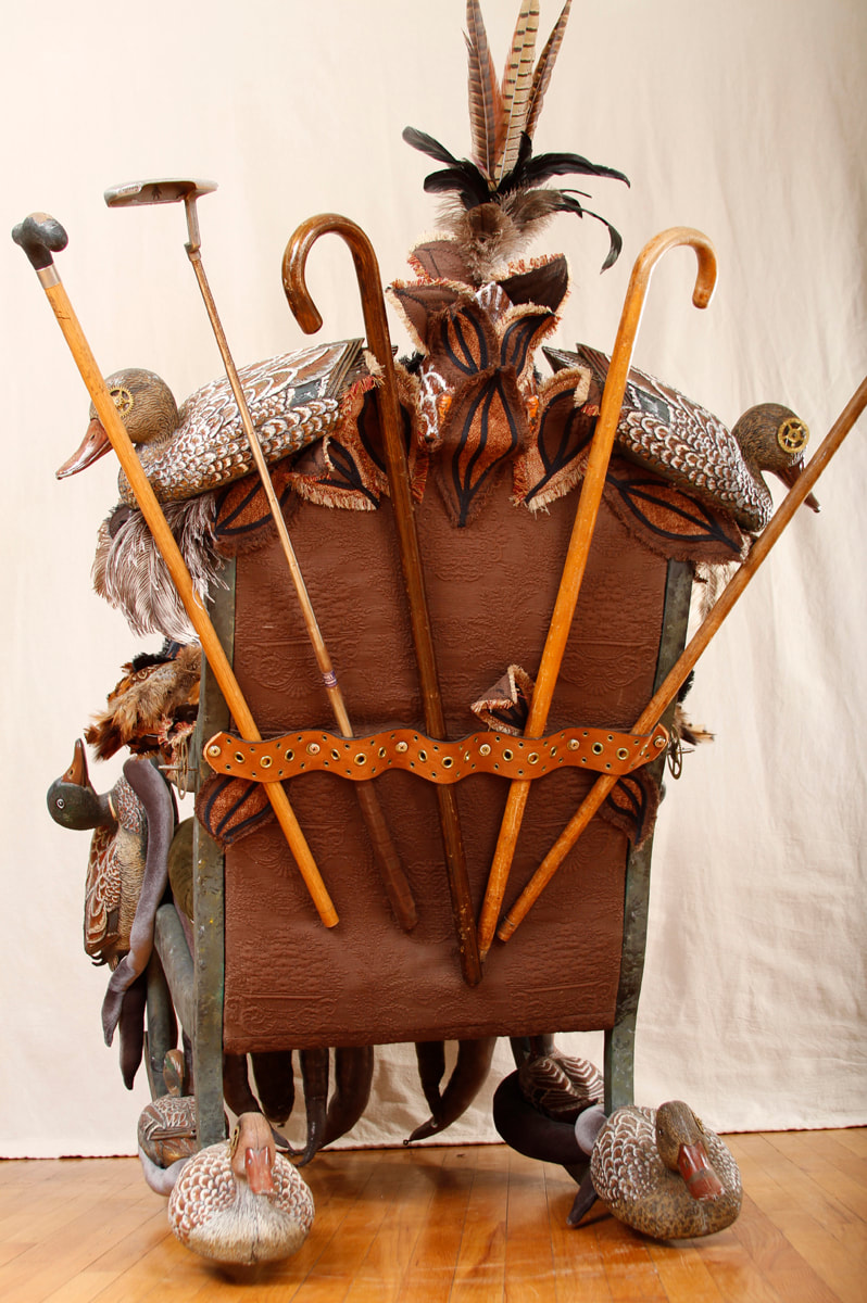 Back view of a rocking chair covered in duck decoys and feathers. The back has a selection of walking sticks, canes, and a golf club.