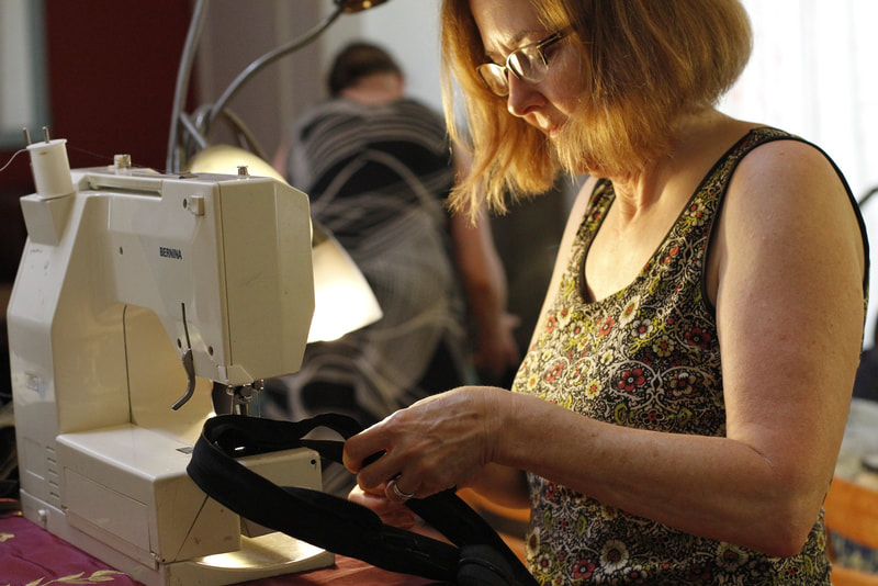 A woman in glasses sews zipper strands together on a sewing machine. 