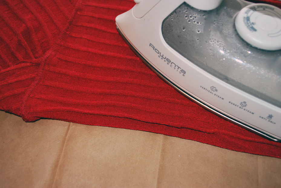 Ironing the red top along the fold to flatten out the top and the paper underneath.