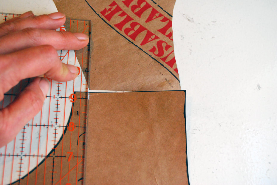 Using a ruler to mark a 1/2" notch in white pencil at the neck edge of the back pattern's shoulder seam.