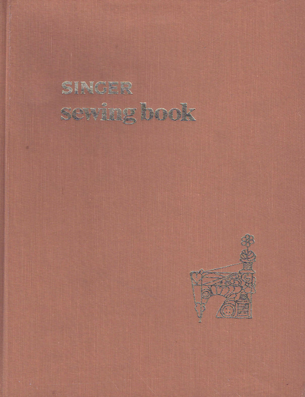 A tan book cover with the text "SINGER sewing book" on the top left and an image of a sewing machine on the bottom right.