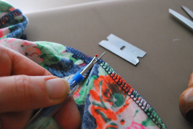 A seam ripper cuts the straight stitches at the base of a 4-thread overlocked seam.