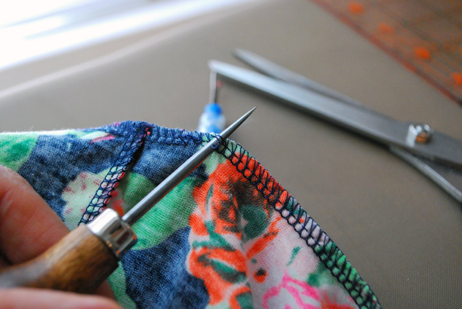 Continuing to use the awl to pull out the straight stitches at the base of a 4-thread overlocked seam.