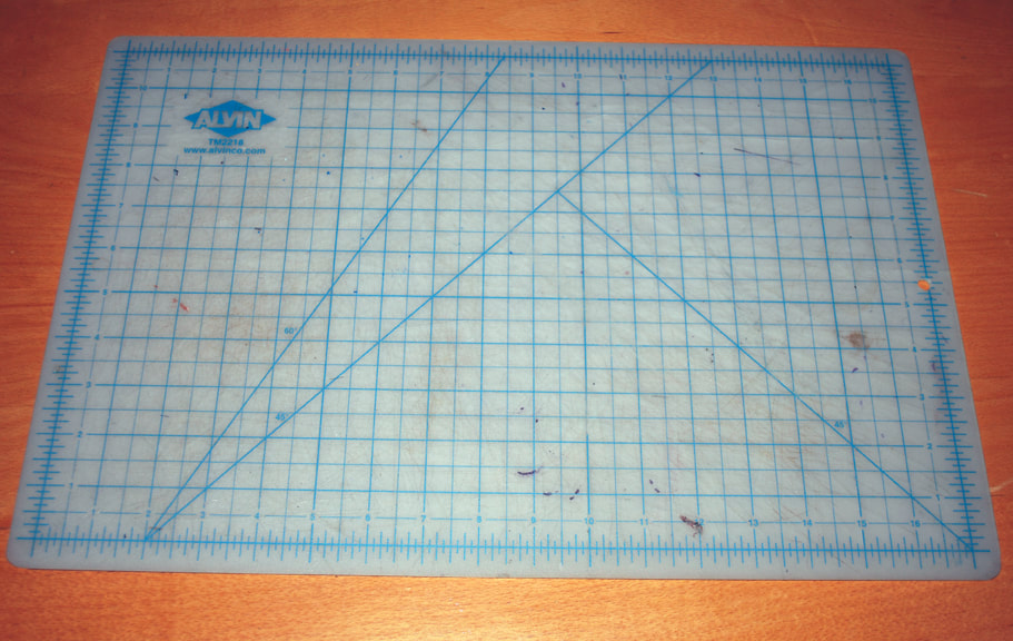 And off white cutting mat gridded with blue lines lays on a wooden table.