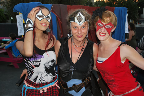 Three women with masks and colorful costumes smile for the camera.