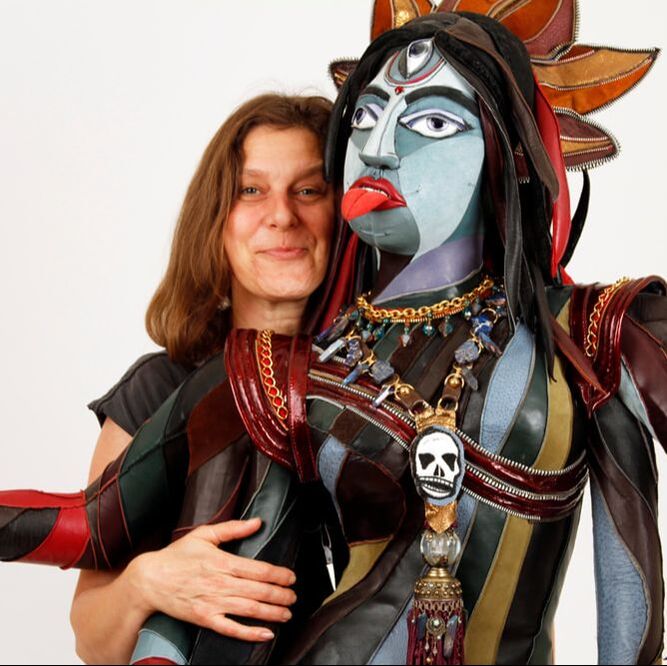 A woman with light brown hair holds the arms of a brightly colored representation of the goddess Kali.