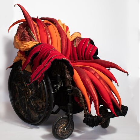 Black and copper wheelchair with a padded, spiked seat cover in orange, red, and gold.