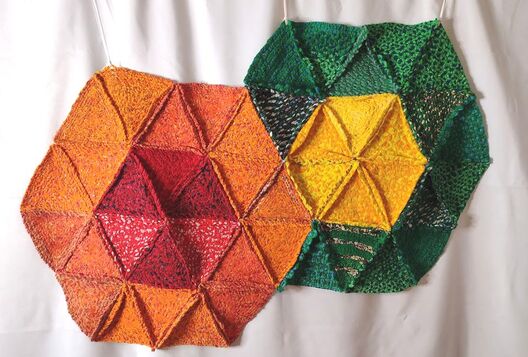Two hexagonal rag rugs made up of triangles combined together. One is orange with a red center, the other is green with a yellow center.