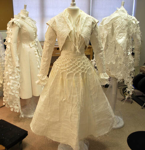 Three white paper costumes on dress forms