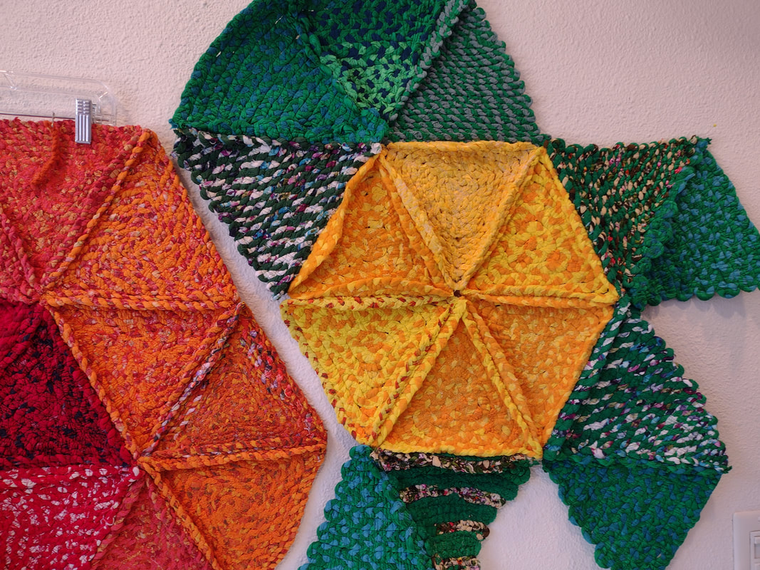Two rag rugs made up of triangles sewn together, one in orange and red and the other in yellow and green.