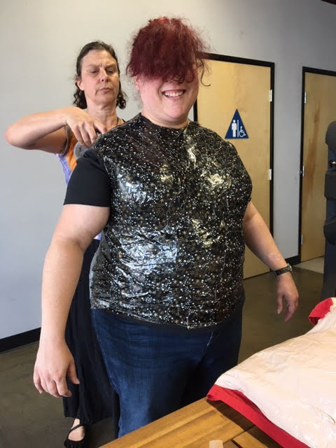 A woman with an intense expression duct tapes all around a woman's torso to create a dress form.