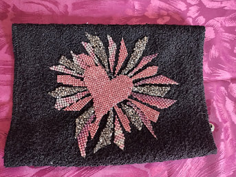 A pink jewel heart on black fabric surrounded by an explosion of pink and grey jeweled shards