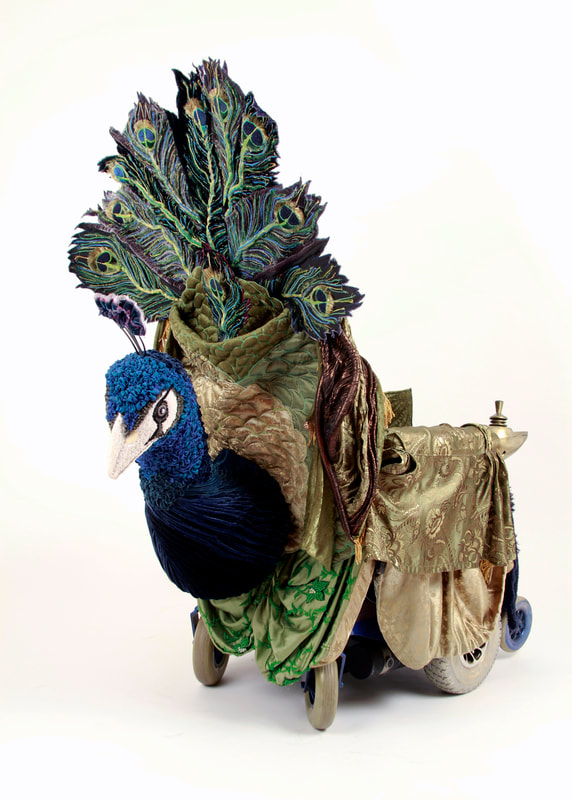 An Art Nouveau style peacock is built into a mobility scooter. The peacock is in shades of green , gold, and blue, and is mounted to the back of the scooter. 