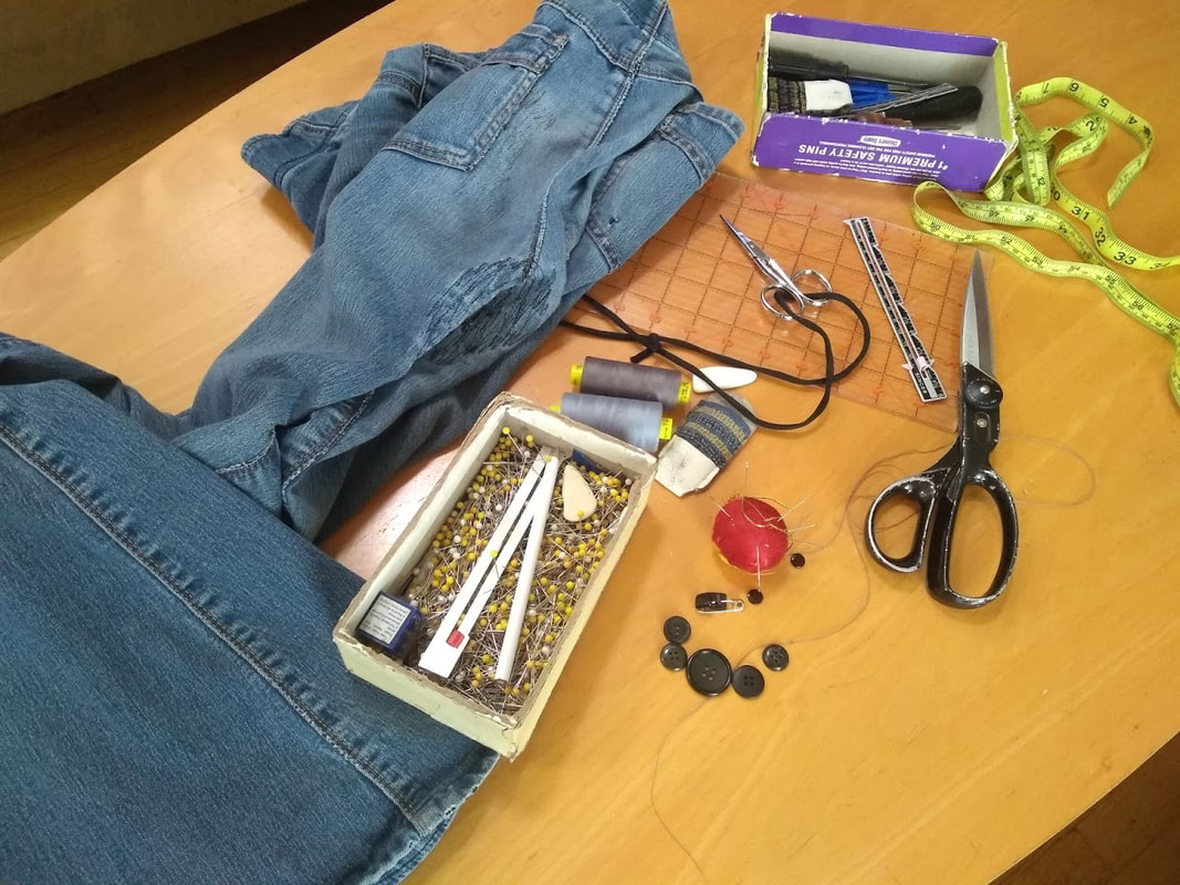 Mending and sewing supplies and a pair of heavily repaired blue jeans on a table 