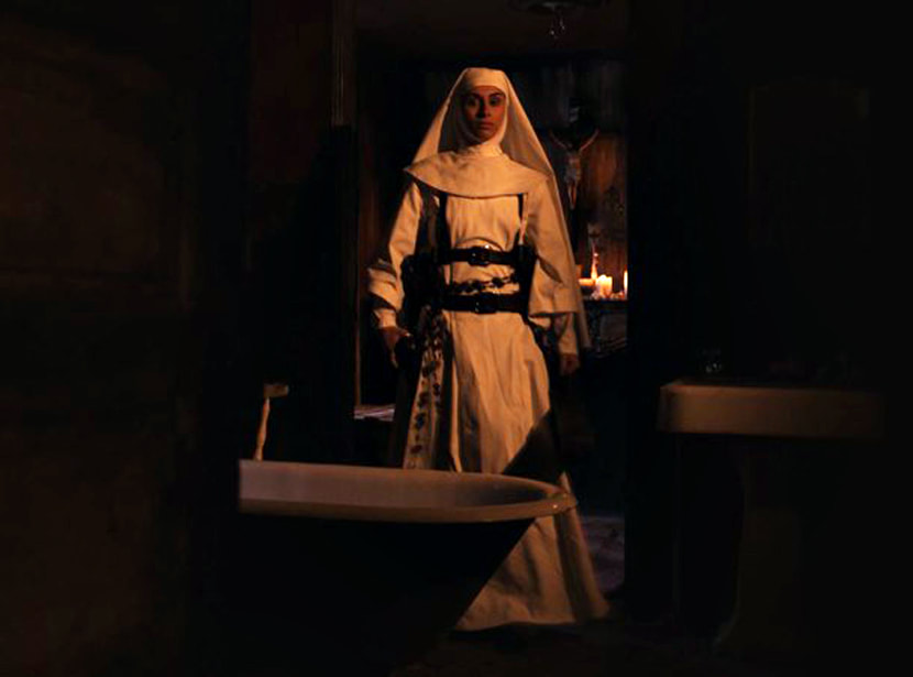 A nun in white with a huge set of rosary beads pulls out her gun.