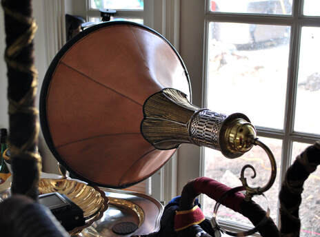 A groamophone horn made out of leather, a lampshade, and a lamp sconce sits above a silver platter.