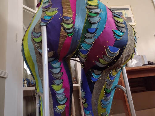 A sculpted bottom covered in multi-colored swirls of fabric with pinned on rows of contrasting scales