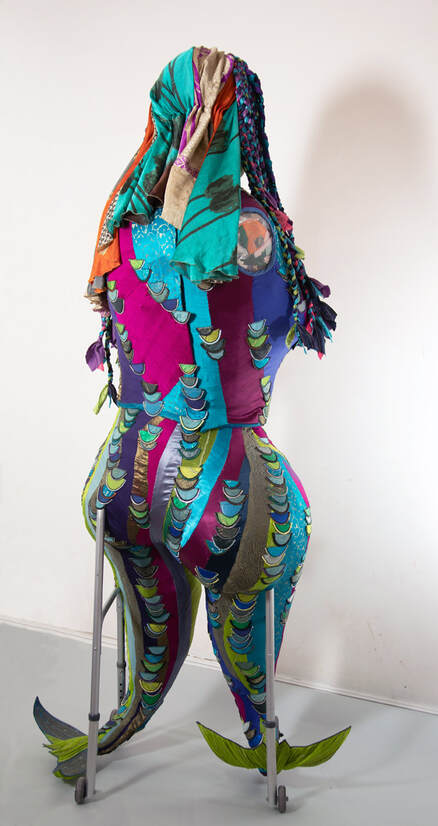 Back view of an armless sculpture of a woman with colorful legs/fishtails built into a walker.