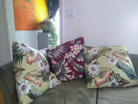 Three Hawaiian floral print pillows on a sage green sofa. 