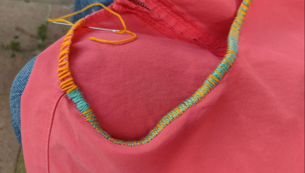 Coral colored top with orange and turquoise embroidery being sewn around the neck edge.