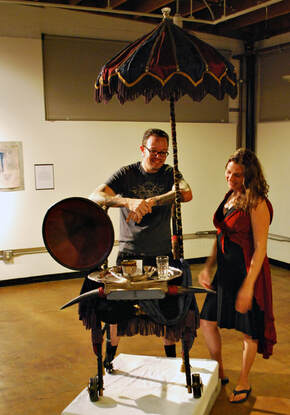 A man and a woman look at a walker decorated with cow horns, a parasol, a gramophone horn, and cow horns.